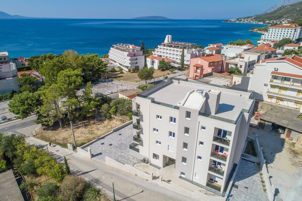 A coastal urban area with modern buildings, a clear blue sea, and a hilly landscape in the background. - Altiora Prestige Residence 205 (Gradac)