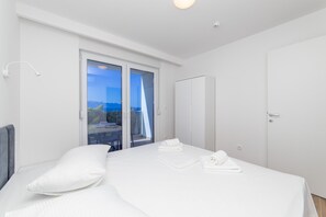 A modern bedroom with a large bed, a wardrobe, and a sliding glass door leading to a balcony. - Altiora Prestige Residence 102 (Gradac)