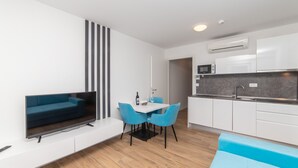 A modern living room with a flat-screen TV, blue sofa, and dining area with chairs. - Altiora Prestige Residence 202 (Gradac)