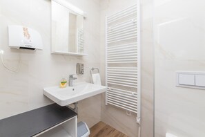 Un baño con lavamanos blanco, espejo, toallero y radiador blanco.