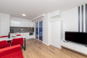 Eine moderne Küche mit weißen Schränken, ein Essbereich mit roten Stühlen und ein Flachbildfernseher an einem weißen Schrank befestigt.