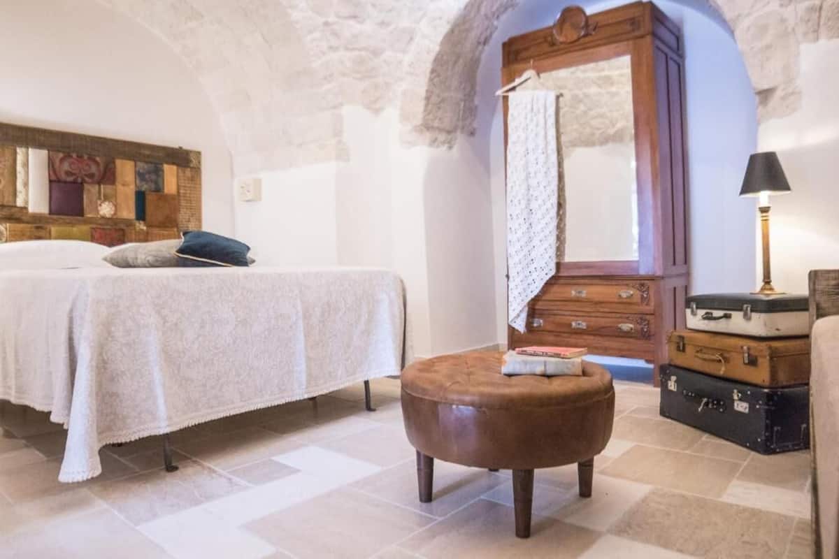 A bedroom with a bed, a wooden dresser, a bench, and a mirror.