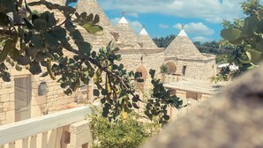 A stone building with multiple conical roofs, surrounded by greenery. - Navolte Trulli e Piscina (Locorotondo)