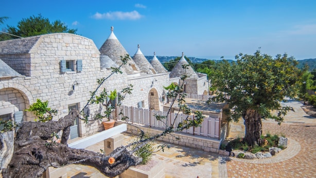 A stone building with multiple conical roofs, a tree, and a paved courtyard. - Navolte Trulli e Piscina (Locorotondo)