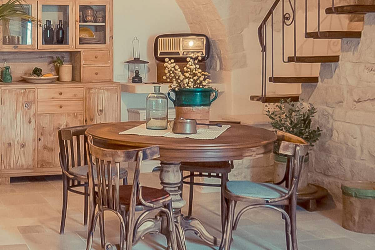 A dining area with a wooden table and chairs, a hanging light fixture, and a staircase with a wrought iron railing.