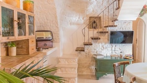 A rustic interior with a stone wall, wooden cabinets, a staircase, a television, and a dining area. - Navolte Trulli e Piscina (Locorotondo)