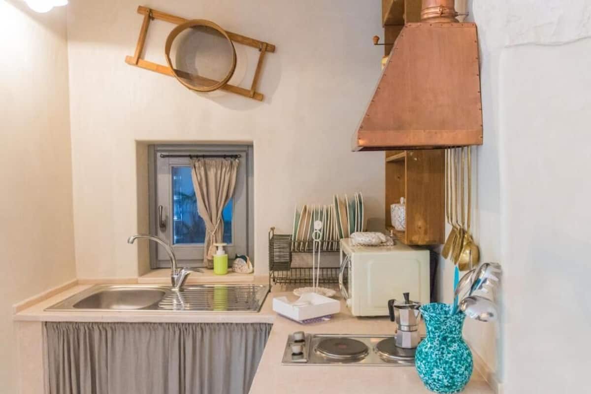 A compact kitchen with a sink, a toaster, a coffee maker, and a hanging pot rack.