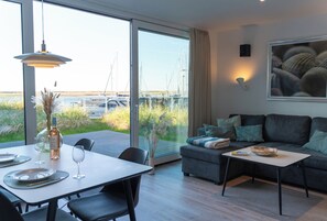 A modern living room with a dining area, large windows with a marina view, and a sofa with cushions. - Spacious Apartment with exceptional Sea View and Wellness Area! (Wendtorf)