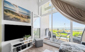 Un soggiorno con televisore, impianto audio e un'ampia finestra vista spiaggia.