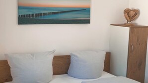 Un dormitorio con cama, almohadas, cabecero de madera, un armario y un cuadro de un muelle.