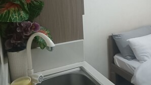 A bathroom with a stainless steel sink, a white toilet, a wooden wall, and a potted plant with purple flowers.