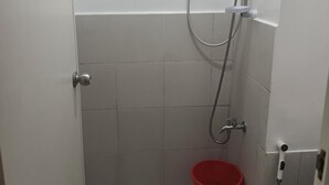 A small bathroom with a toilet, a red bucket, a shower head, and a hand dryer.