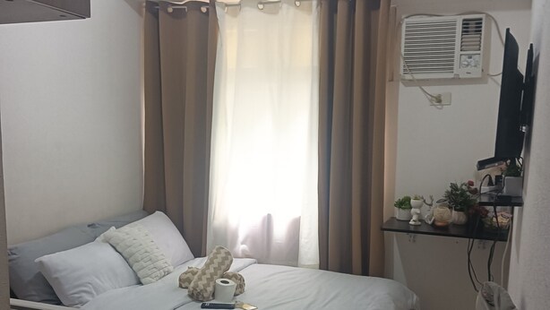 A bedroom with a bed, a desk, a chair, a TV, and an air conditioning unit.