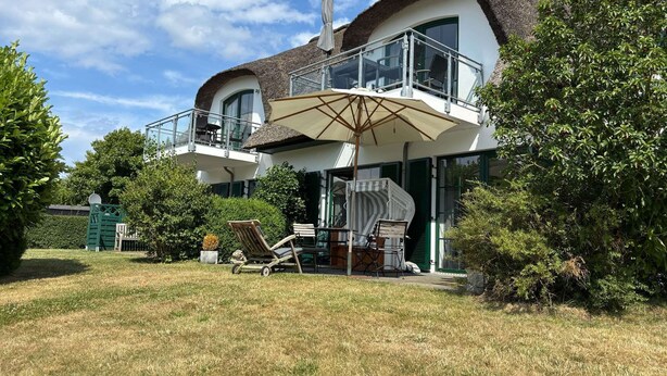Ein zweistöckiges Haus mit Balkon, einem Essbereich mit Gartenmöbeln und einem Garten.