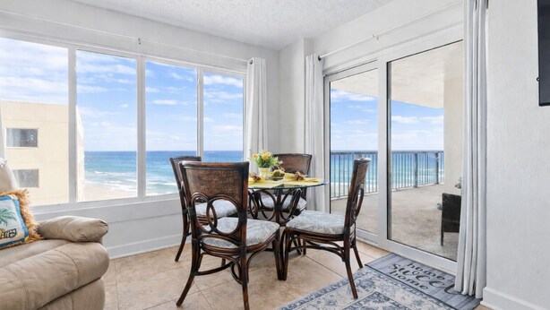 A balcony with a view of the ocean, a dining table with chairs, and a sofa. - Enjoy stunning ocean views from the balcony, living room, dining area, and kitchen. This 2BR condo features a heated beachfront pool, fitness room, king beds in both bedrooms, and comfortably sleeps 4 in beautiful Daytona Shores. (Daytona Shores)