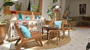 A cozy living room with a round coffee table, wicker chairs, a piano, and a large mirror. - Riad Larbi Khalis Room Essaouira (Marrakesh)