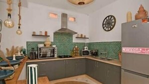 A kitchen with a microwave, stove, and refrigerator. There are cabinets, a clock, and a hanging light fixture. - Riad Larbi Khalis Room Taghazout (Marrakesh)
