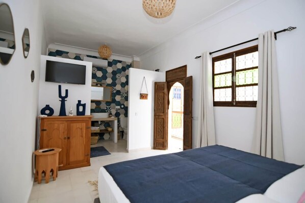 Een slaapkamer met een bed, een televisie, een houten kast en een badkamer die door een open deur zichtbaar is.