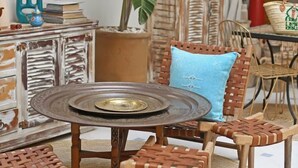 Una habitación con una mesa redonda, sillas de mimbre, una planta en maceta, un espejo y un mueble con diseño rústico.