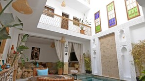 Un área de piscina interior amplia con techo alto, un balcón con barandillas ornamentales y diversas plantas.