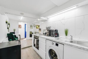 A modern kitchen with a built-in washing machine, a coffee machine, and a sink. - Cosy Little Flat - Perfect Base for Explorers (London)