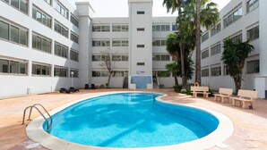 Une piscine entourée d’une terrasse carrelée, agrémentée de bancs et de palmiers.