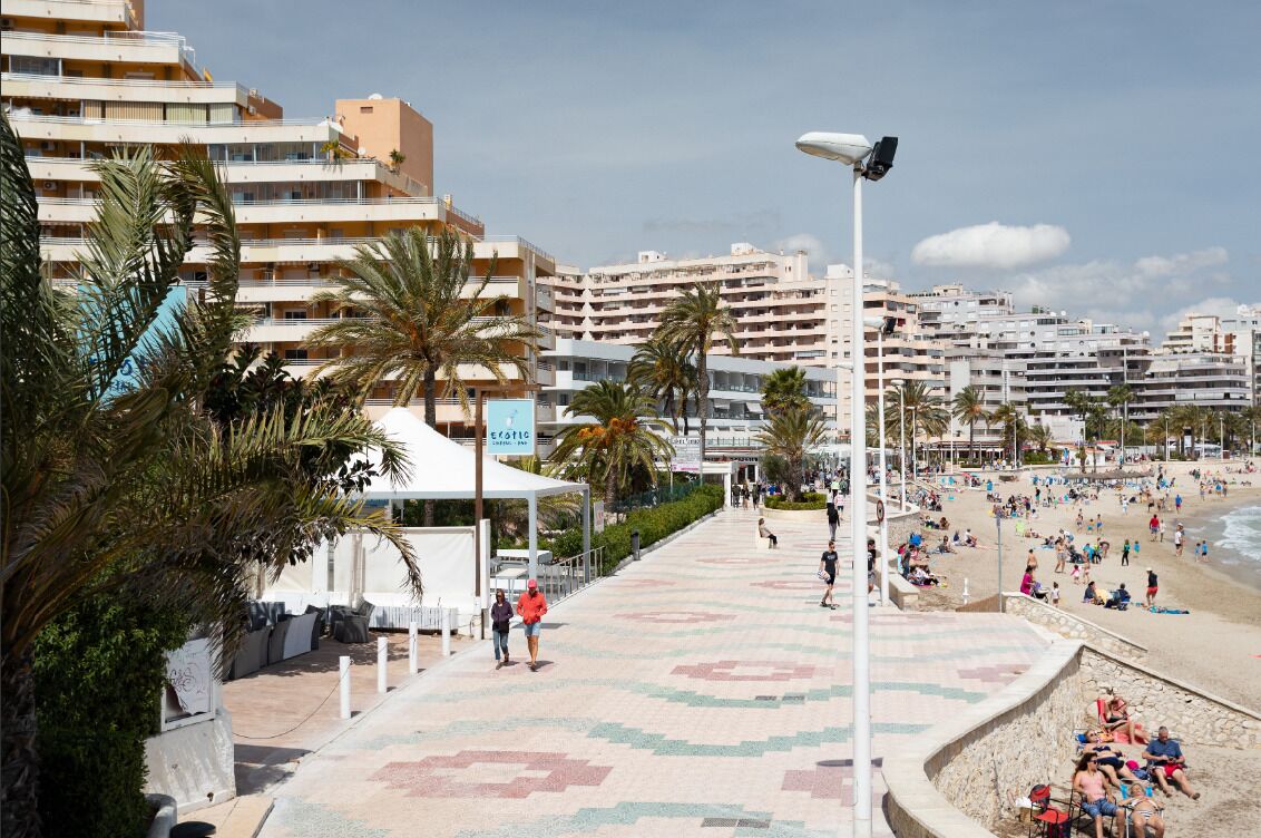 Un paseo marítimo con playa, palmeras y una hilera de edificios de varios pisos.