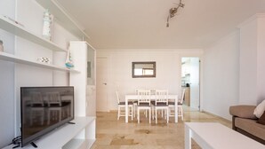 Un salon moderne avec un téléviseur à écran plat, une table à manger avec des chaises, un canapé blanc et un petit meuble blanc.