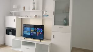 Un salon moderne doté d’un téléviseur à écran plat, de meubles blancs et d’objets décoratifs disposés sur des étagères.