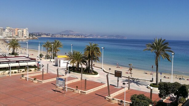 Un paysage urbain côtier avec une plage, des palmiers et un bâtiment portant une enseigne.