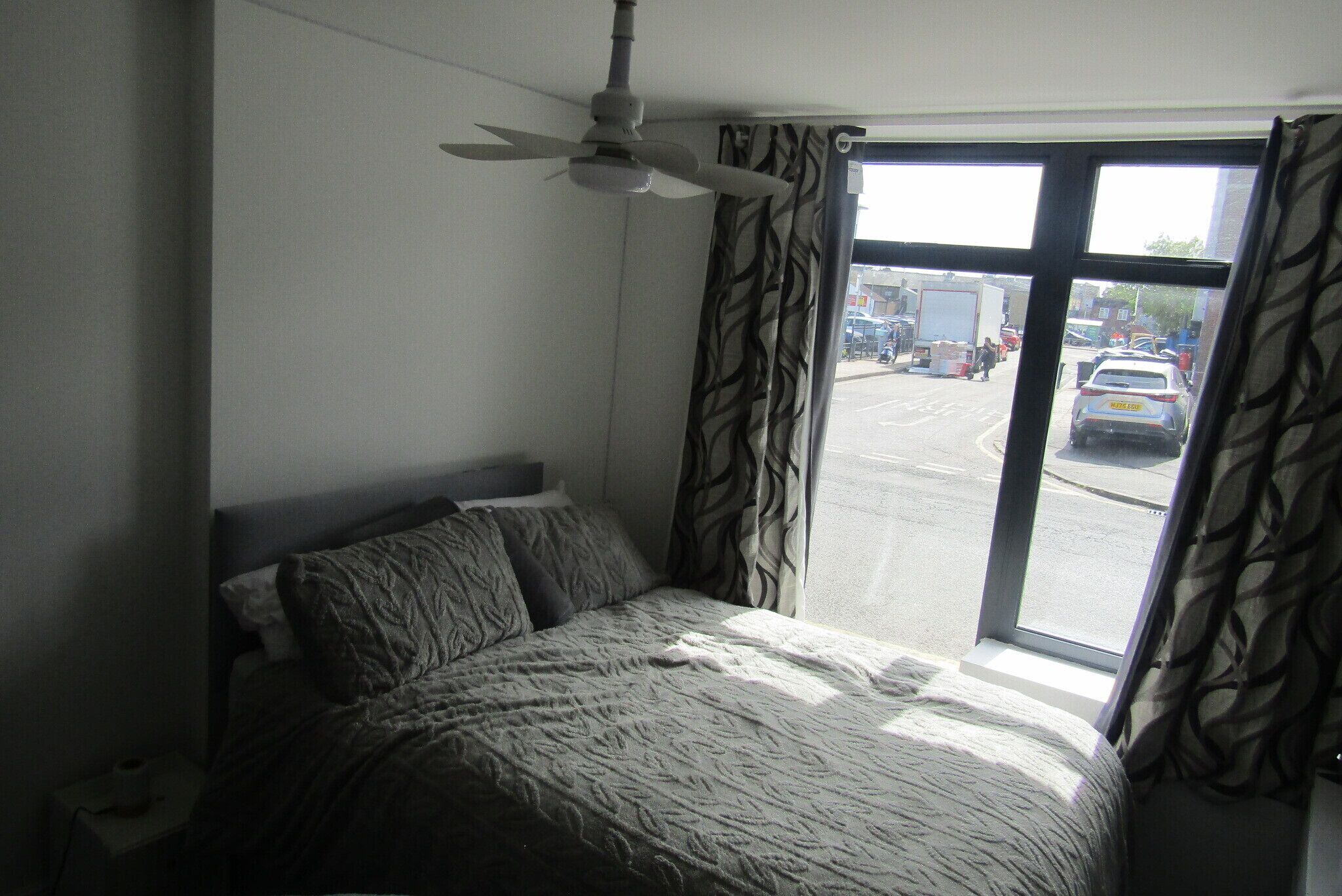 Ein Hotelzimmer mit Bett, Deckenventilator, Vorhängen und Blick auf die Straße.