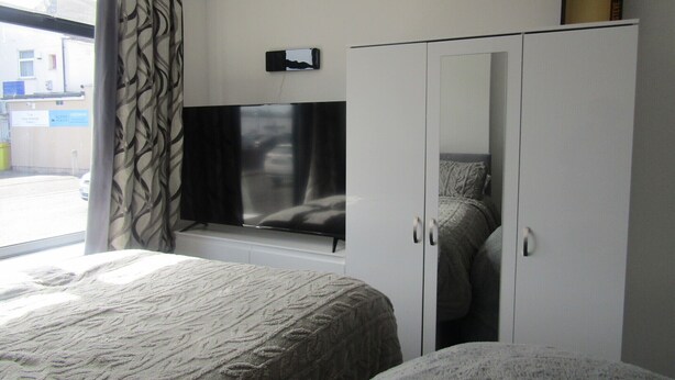 A bedroom with a bed, a wardrobe, a television, and a window with curtains. - Cozy Studio Rental With Private Facilities in Greater London (Welling)