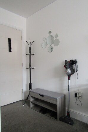 A room with a coat rack, a vacuum cleaner, a bench, and a door. - Cozy Studio Rental With Private Facilities in Greater London (Welling)