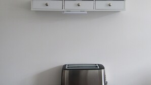 A small dining area with a round table, a toaster, and a white shelf above it. - Cozy Studio Rental With Private Facilities in Greater London (Welling)