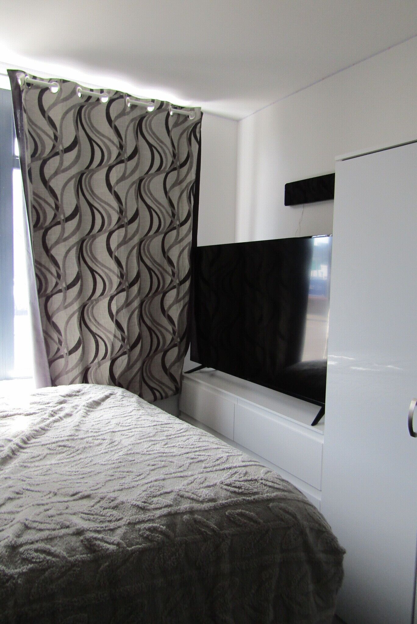 A bedroom with a bed, a TV mounted on the wall, and a window with curtains.