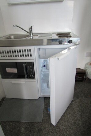 A compact kitchenette with a sink, microwave, and refrigerator. - Cozy Studio Rental With Private Facilities in Greater London (Welling)