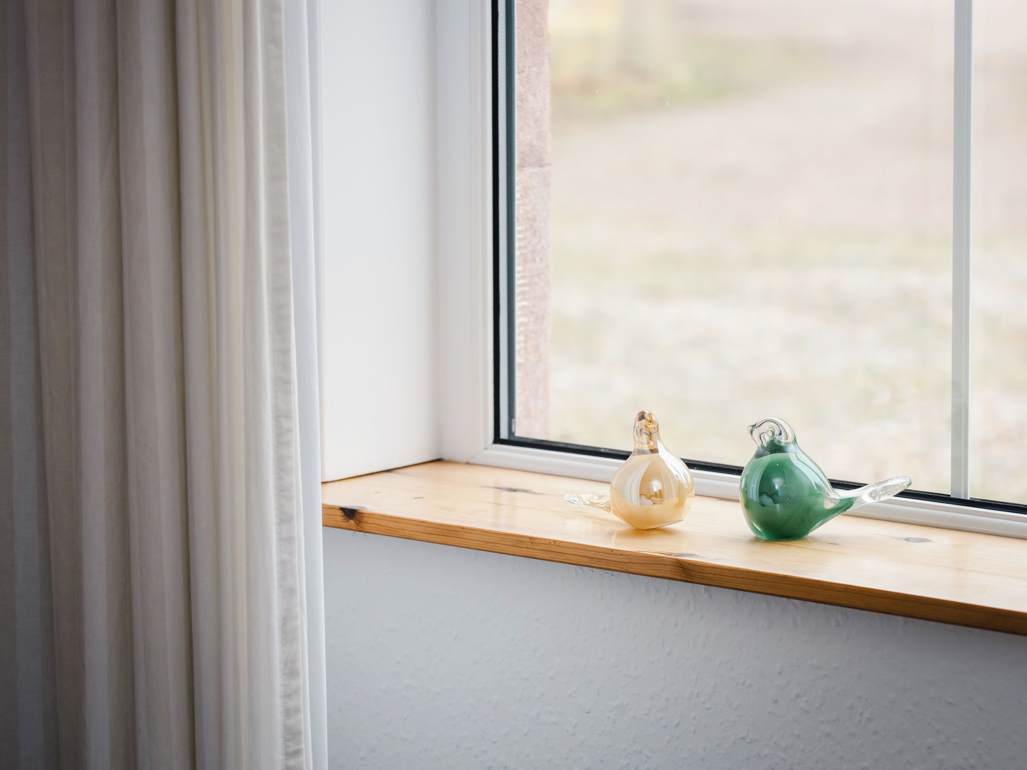 A window with a wooden ledge, two glass bottles, and a view of a garden.