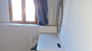 Une pièce avec une fenêtre, une chaise, un bureau avec des tiroirs et un miroir au mur.
