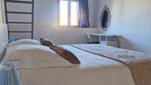 Une chambre à coucher avec un lit, un bureau, une échelle, une fenêtre avec des rideaux et un miroir sur le mur.