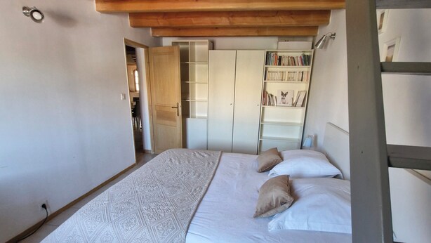Une chambre à coucher avec un lit, un plafond en bois, une bibliothèque et une porte donnant sur une autre pièce.