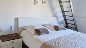 Une chambre à coucher avec un lit, une table de chevet, une lampe, une échelle et des tableaux encadrés accrochés au mur.