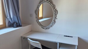 Un bureau blanc avec une chaise, un miroir et une fenêtre avec des rideaux.