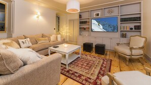 Una sala de estar con sofá, una mesa de centro, televisor y estantería.
