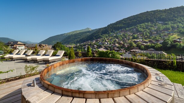 Un jacuzzi con terraza de madera, sillas reclinables y vistas a un pueblo en la ladera.