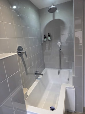 Een moderne badkamer met een badkuip, douche en betegelde wanden.