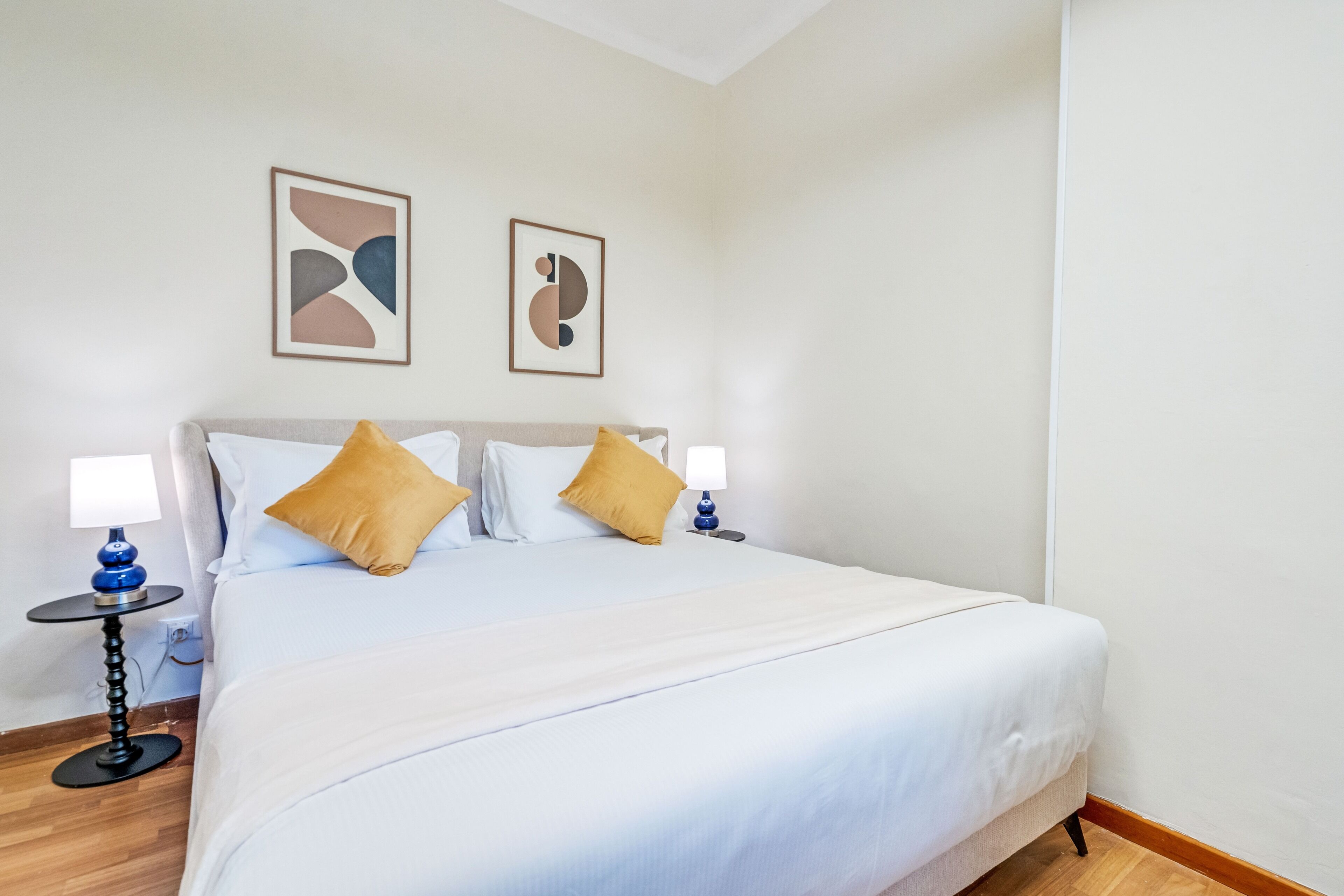 A neatly arranged hotel room with a large bed, two bedside tables with lamps, and abstract wall art.