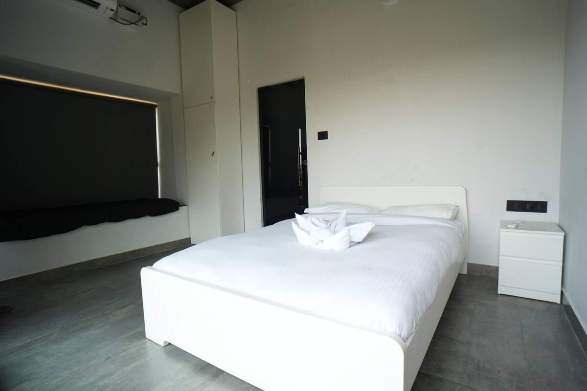Un dormitorio moderno con una cama grande, una mesita de noche, un armario y un banco empotrado en la pared.