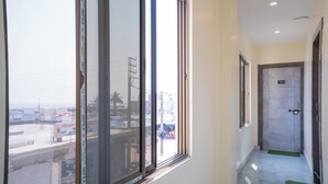 A hallway with large windows, a door with a number plaque, and a green mat on the floor. - Mahabhoj Hotel & Restaurant (Mandarmani)