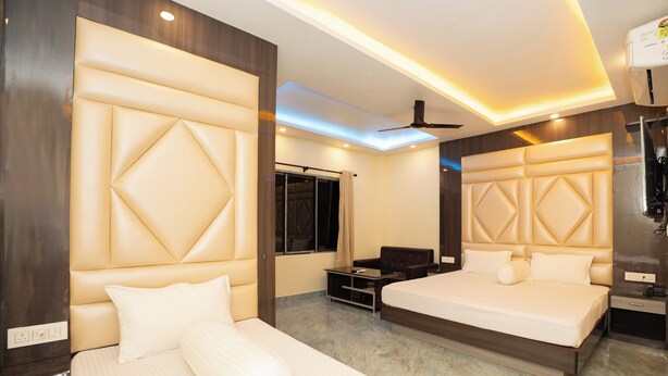 A modern hotel room with a large bed, a seating area, a TV, and a wardrobe. - Mahabhoj Hotel & Restaurant (Mandarmani)