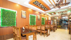 A dining area with wooden tables and chairs, green wall decorations, ceiling fans, and framed artwork. - Mahabhoj Hotel & Restaurant (Mandarmani)